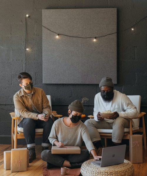 Three coworkers wearing masks on a Surface laptop with Christmas presents on a cart